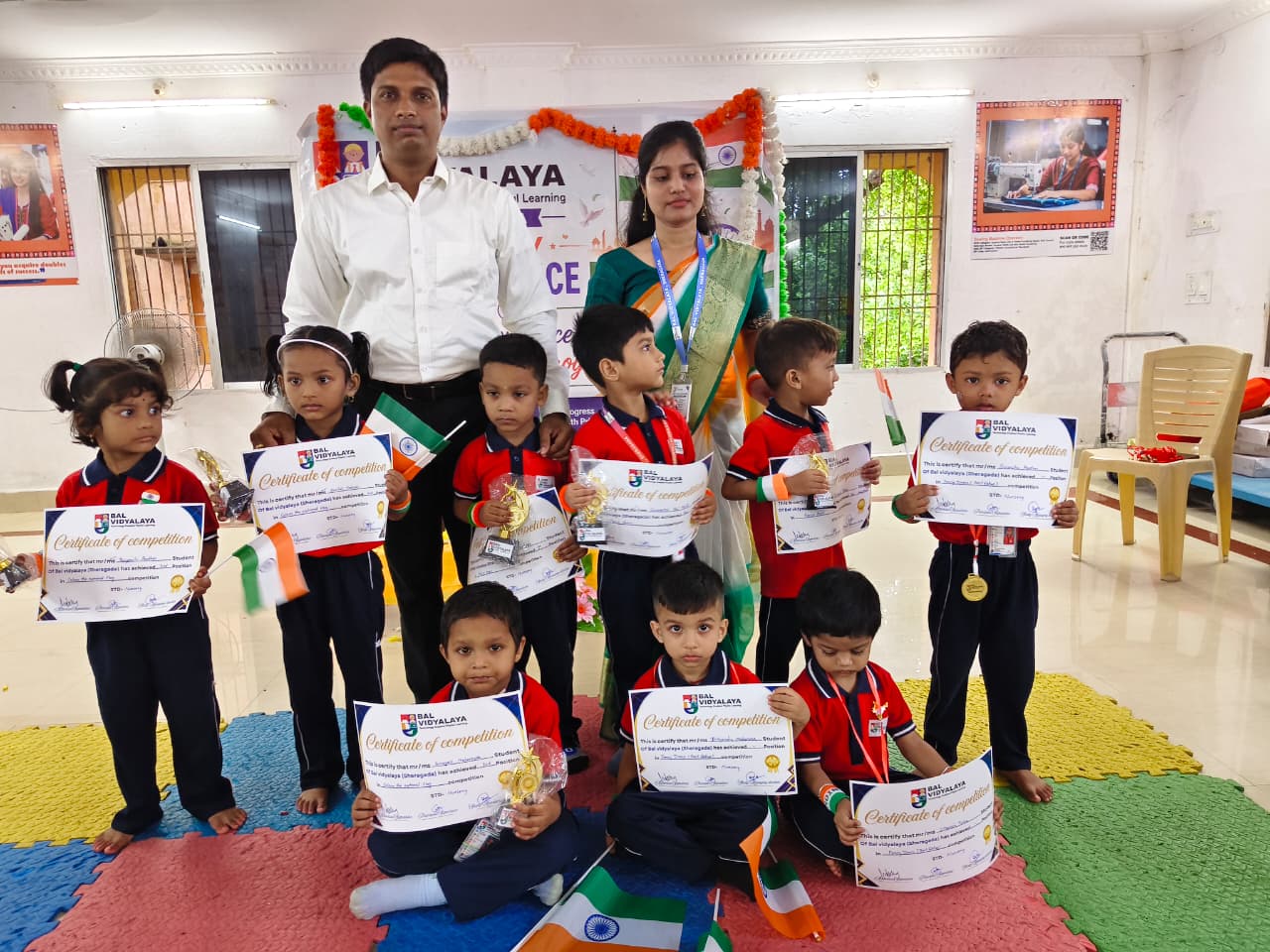 Children with certificates of competition, trophies and flags at Bal Vidyalaya